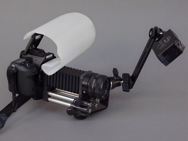 <b>完成したシステムだが、ガンダムに出てくるモビルアーマーみたいになった（笑）。K-5の内蔵ストロボには自作ディフューザーを被せ、さらにボール雲台やブラケットなどを組み合わせスレーブストロボ「ヒカル小町」を装着。スタジオ撮影用の照明セットをカメラにくっつけた状態だが、これで手持ち撮影が可能になる</b>