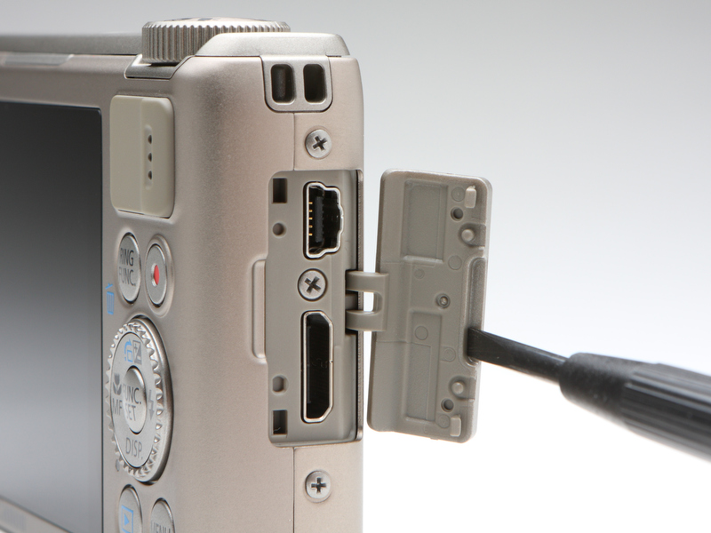 <b>インターフェースはAV-OUTを兼ねるUSB端子とHDMI端子の2つが備わる。端子の上の縦に２つ並ぶ穴はストラップ取り付け用で、反対側の側面にも備わっている</b>