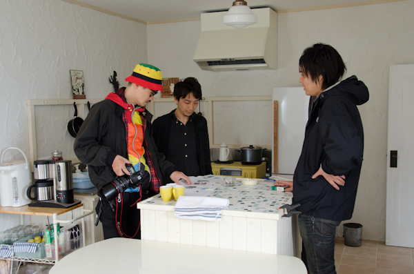 <b>進行表をチェックしながら撮影順序の検討は天気との戦いでもある。日中シンクロのストロボの配置や光量は写真の決めてにもなるので慎重にセッティングされる。スタジオや屋内ロケの必需品、空気の抜けたテニスボールは三脚やスタンド類の下に挟んで床面をガードする</b>