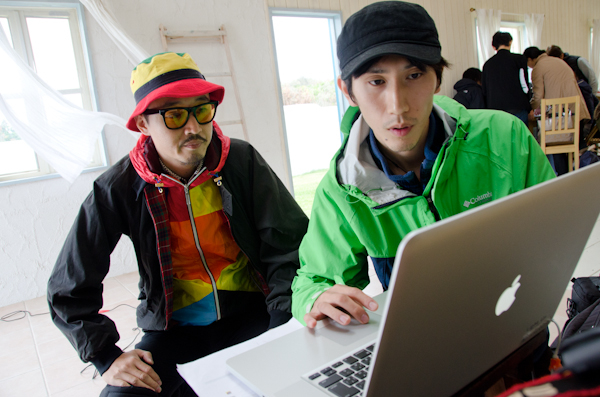 <b>進行表をチェックしながら撮影順序の検討は天気との戦いでもある。日中シンクロのストロボの配置や光量は写真の決めてにもなるので慎重にセッティングされる。スタジオや屋内ロケの必需品、空気の抜けたテニスボールは三脚やスタンド類の下に挟んで床面をガードする</b>