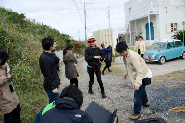 <b>膝のプロテクターは彼のロケでは必ず必要になる。サバイバルゲーム用品の流用らしいが、膝をついて撮影が多いので重宝しているらしい。直結したMacでのピントのチェックは大事な役目だ。ボクもそうだが、撮影に夢中になっていると構図やシャッターチャンスが優先になりがちなので、開放近くだとピントの範囲が狭いのでオペレーションしてもらったほうが正確でよい</b>