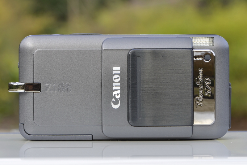 <b>レンズバリア（カバー）の黒っぽいパーツは、スライドさせる際に指をかけるような形状になっている。……が、正直言ってコレは使いモノにならない。そう、指先に吸盤でもないかぎり開けない（笑）。ということで、右手の人差し指と中指で「Vの字」を作って、その指をバリアの上下にかけてグワシッとスライドさせるのが正解!</b>