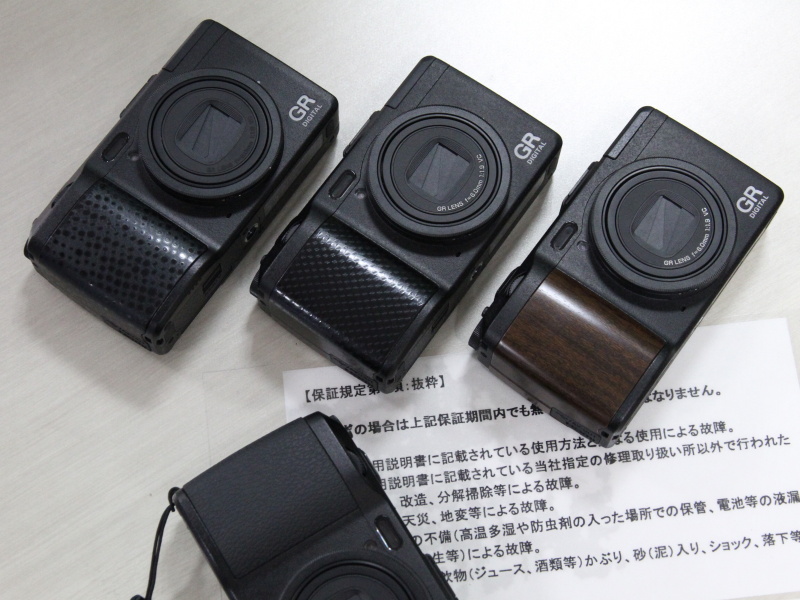 <b>グリップ交換のサンプル。奥の左から「レザー」、「カーボン」、「ウッド」。手前は筆者が持参した素のGR DIGITAL IV</b>