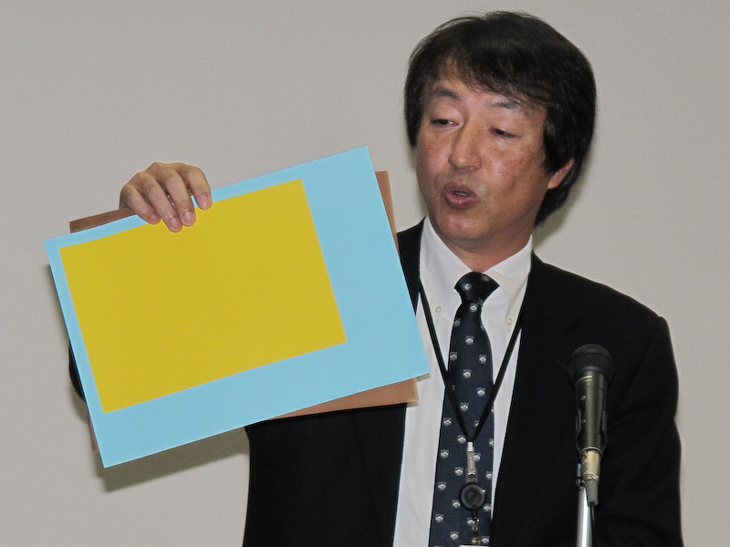 <b>ソニー業務執行役員SVP 半導体事業本部 イメージセンサ事業部 事業部長の上田康弘氏。手にしているのは従来のCMOSセンサーをイメージした紙。黄色がセンサー、水色が画像処理回路、茶色が支持基板に当たる</b>