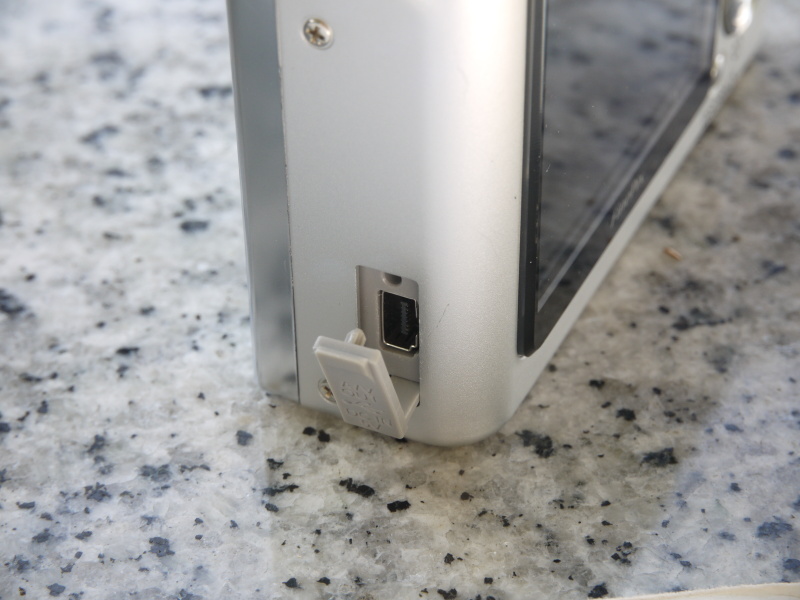 <b>ストロボ側の側面下部には「マルチコネクターアダプター接続端子」あり。ここにマルチコネクターとACパワーアダプターを接続してバッテリーを充電する。反対（グリップ側）の側面には「ストラップ取り付け部」がある。この取り付け部、自由に回転するちょっと凝った作り（?）になっている</b>