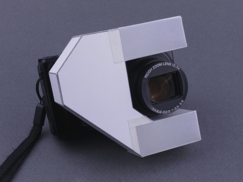 <b>完成したディフューザーをCX6に装着したところ。レンズの上下に2カ所の発光部がある。昔からある一眼レフ用の「2灯式マクロストロボ」と同じだが、内蔵ストロボの光を内部の反射板で導いているのが、ミソ。つまりこのカメラのセットは“ノンフレックス”ではない（笑）</b>