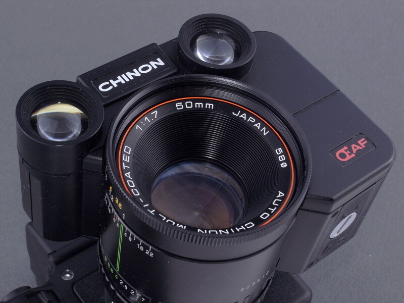 <b>レンズ前面を右下から見たところ。レンズそのものはチノンのMF標準レンズ「50mm F1.7」の転用である。向かって右下には、単4電池が3本の挿入口がある。AFメカはプラボディだがレンズ鏡筒は金属製で、全体にがっちりとした作りでそれなりに高級感がある。</b>