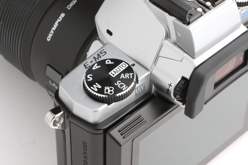 <b>撮影モードダイヤルはトップカバーの左側に置かれる。ロック機構があると、不用意に動かないように思える。“ペンタ部”側面の横長の穴は、動画撮影用のマイク。</b>