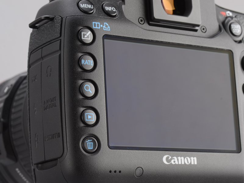 <b>液晶モニター左横に並んだボタンは青色の再生系スイッチが増えた。虫眼鏡アイコンボタンは、再生画像の拡大/縮小を行うためのもの。再生時に画像のお気に入りレベルを付加できる[RATE]レーティングボタンが目新しい。また、5D Mark IIではピクチャースタイルへのダイレクトアクセスボタンがあったが、5D Mark IIIではそれがクリエイティブフォトボタンに進化し、ピクチャースタイル、多重露出、HDRへの入り口となる。</b>