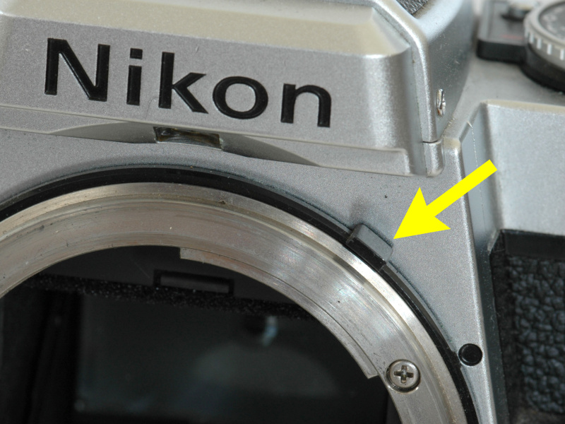 <b>Ai方式のボディ（ニコンFE2）。矢印の部分に「露出計連動ガイド」が当たって絞り値をボディに伝える</b>