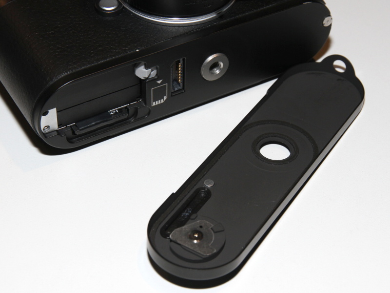 <b>ライカMのベースプレート。キーおよびボディに引っ掛ける部分の形状が変更。無線LANメモリーカードを使用する際、真鍮は電波を通さないため一部を樹脂製としている（穴のように見える部分）。三脚穴はカメラボディ側に移設</b>