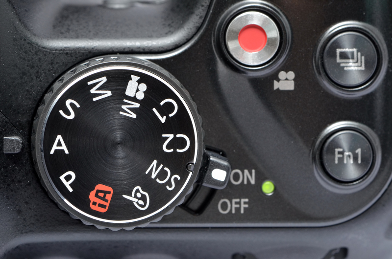 <b>上面のモードダイヤル周辺のボタン配置は、基本的にDMC-FZ150を踏襲している。が、電源スイッチのあった場所にはFn1ボタンが配置され、電源スイッチはモードダイヤル基部に移動した。</b>