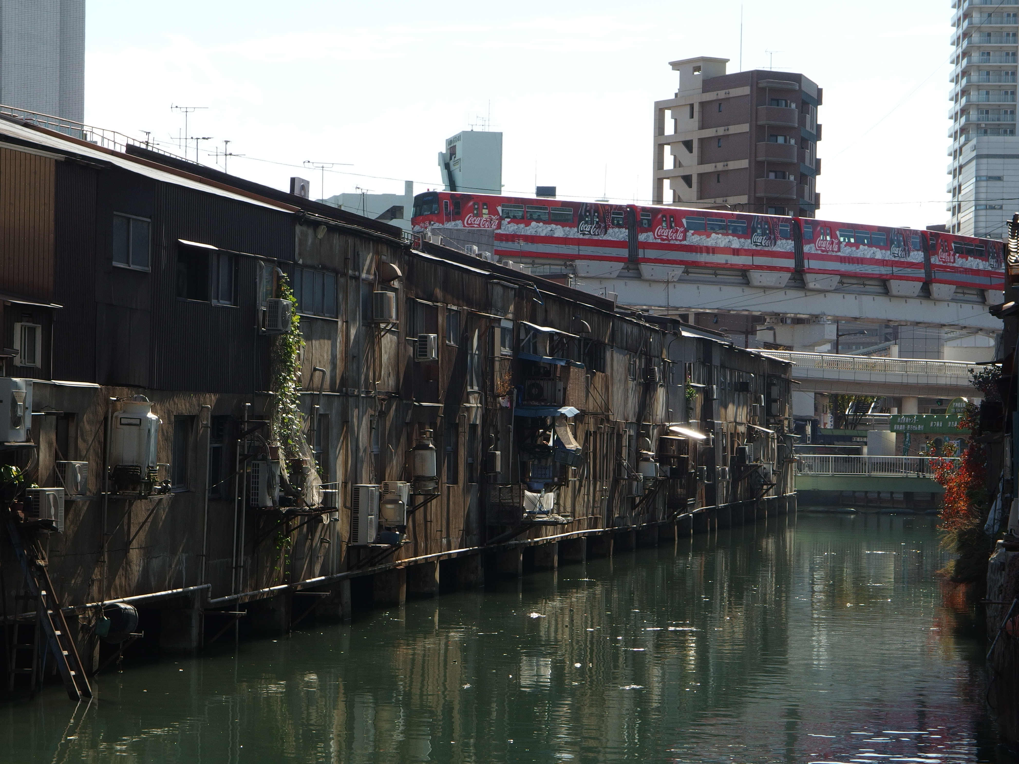 <b>すぐ脇を流れる神獄川の上にせり出している旦過市場の向こうを近代的なモノレールが横切っていく。XZ-2 / 約6.5MB / 3,968×2,976 / 1/400秒 / F5.6 / -0.7EV / ISO100 / WB:くもり / 21.4mm</b>