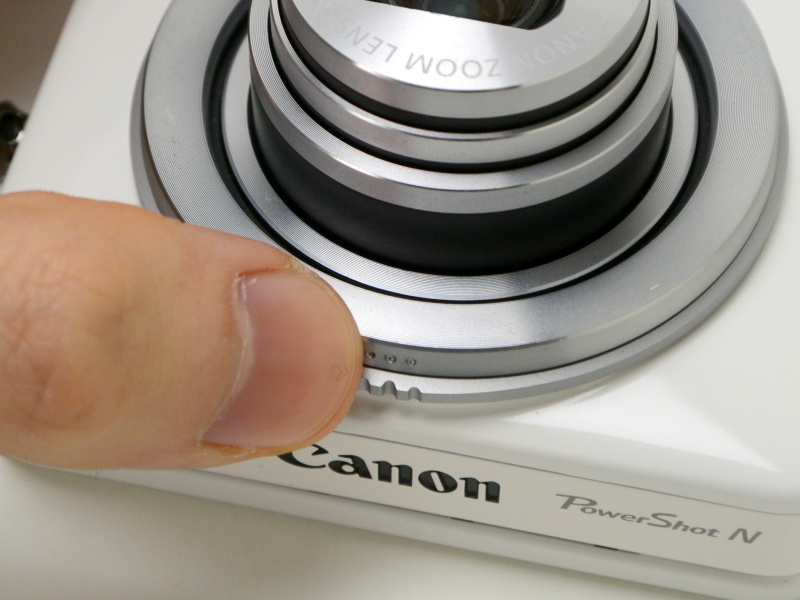 シャッターリング（「…」のマーク）を押し込んだところ（右）。反対側からも押せる。ストロークはコンパクトデジカメのシャッターボタンに近く、半押しも可能