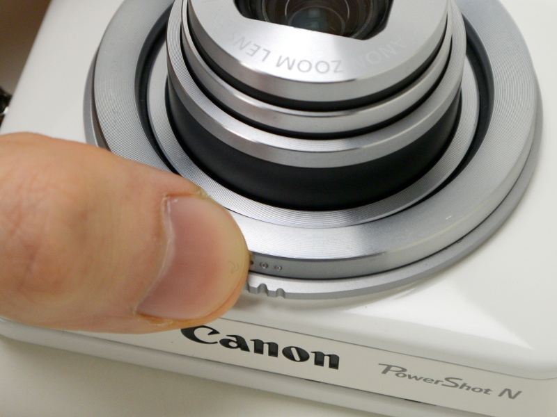 シャッターリング（「…」のマーク）を押し込んだところ（右）。反対側からも押せる。ストロークはコンパクトデジカメのシャッターボタンに近く、半押しも可能