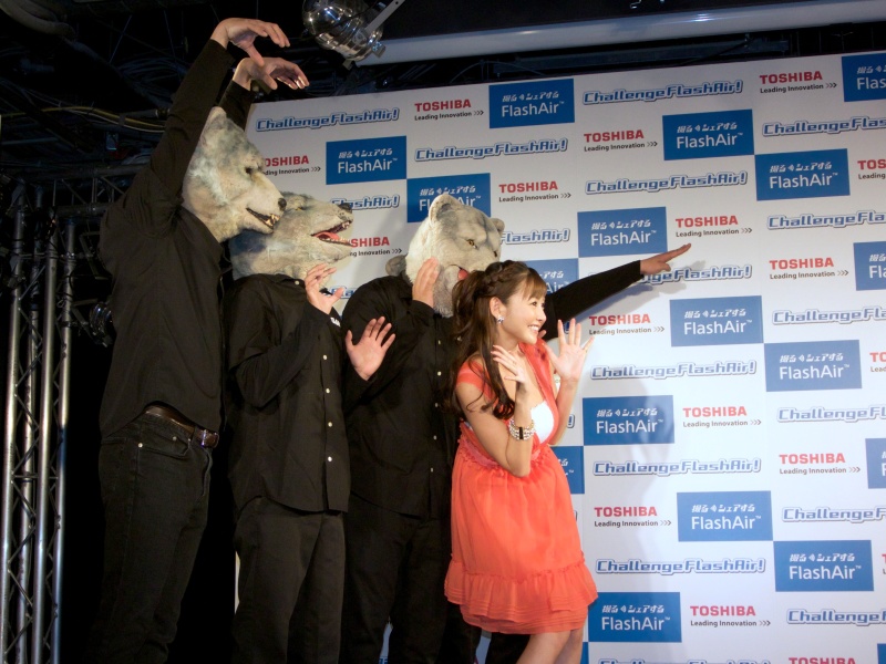 ジャンケン・ジョニーさん（右）が杉原さんとバンドメンバーを撮影。司会者のスマートフォンにその撮影画像が転送される様子をデモンストレーションした