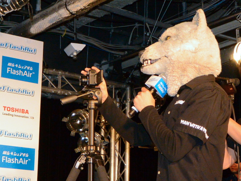 ジャンケン・ジョニーさん（右）が杉原さんとバンドメンバーを撮影。司会者のスマートフォンにその撮影画像が転送される様子をデモンストレーションした