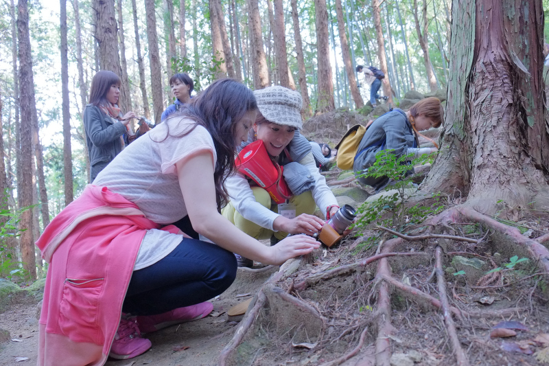 熊野古道を歩きながら、参加者の疑問に答えたり、カワイく撮るコツを伝授する山本まりこさん。ただいま、カワイイ玉ボケの作り方をレクチャー中。