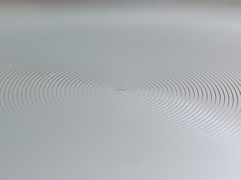 フレネルレンズそのものを拡大して見ると、同心円状の溝が刻んであるのがわかる。通常のレンズを同心円状に分割し、平面に再配置した構造になっているのだ。