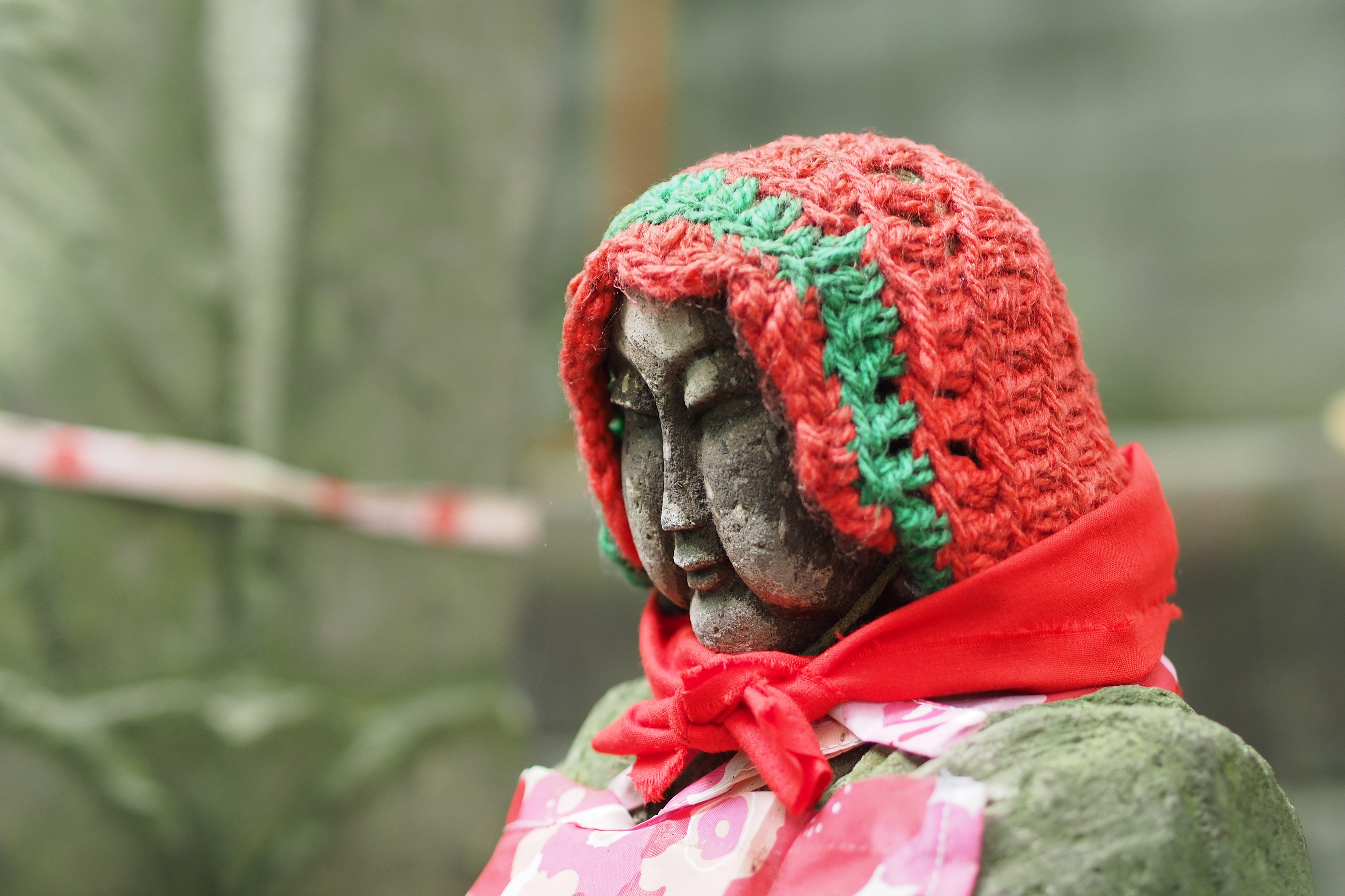 おおかたはお手製の前掛けを付けているだけだが、中には毛糸の帽子（頭巾？）をかぶっている石仏もある。M.ZUIKO DIGITAL 45mm F1.8 / 1/25秒 / F2 / +0.3EV / ISO400 / 絞り優先AE / WB：晴れ / 45mm