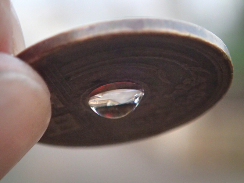 5円玉の穴に水滴を垂らすと、表面張力によってご覧の通りのレンズができる。これで5円玉レンズが完成する。