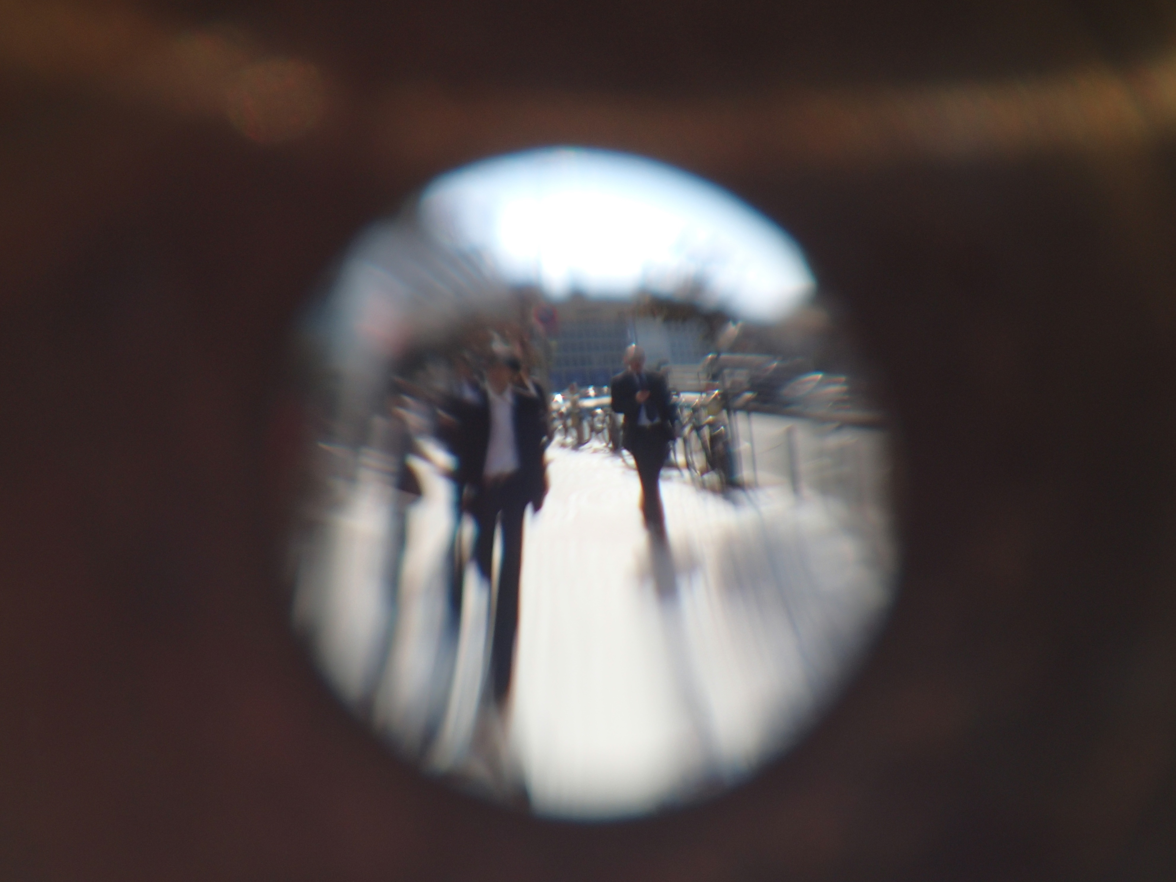 同じく新宿西口での撮影。画面の中央にのみピントが合い、周辺部はピンボケで、下部では像が流れて人物の足が伸びている。何枚か撮るうちに水が蒸発するので描写も変わり、そのうちレンズそのものが消えてしまう。