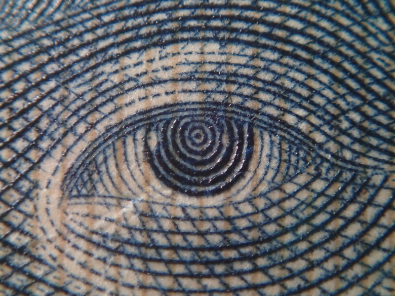 スーパーマクロモードで望遠100mm相当にズームすると、千円札の野口英世の目がこの大きさに写る。撮影範囲が狭いのでストロボの光は回っているように見えるが、感度をISO400まで上げなければ露出不足になってしまう。