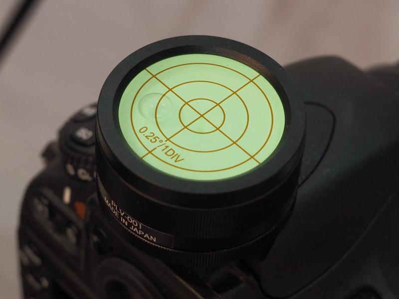 カメラ用精密水準器PLV-001の装着例。0.25度の傾きも計測できるというのが特徴。蓄光機能により、数秒間ライトで照らすとしばらく発光する。本体はアルミ削り出し