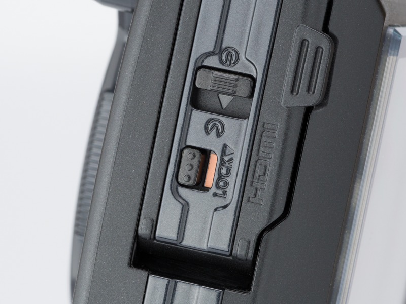 側面の端子カバー。底面の電池/カード室のカバーと同じくロックレバー付き。写真はロック解除状態。