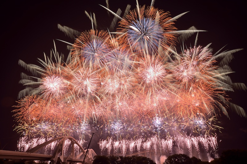 「夕映えの椰子」と名付けられたワイドスターマイン。洋火の橙色はホワイトバランス電球が良い。D600・AF-S NIKKOR 18-35mm f/3.5-4.5G ED・マニュアル露出・F13・1.8秒・WB:電球・ISO100・ND4フィルター　リモートケーブル・三脚