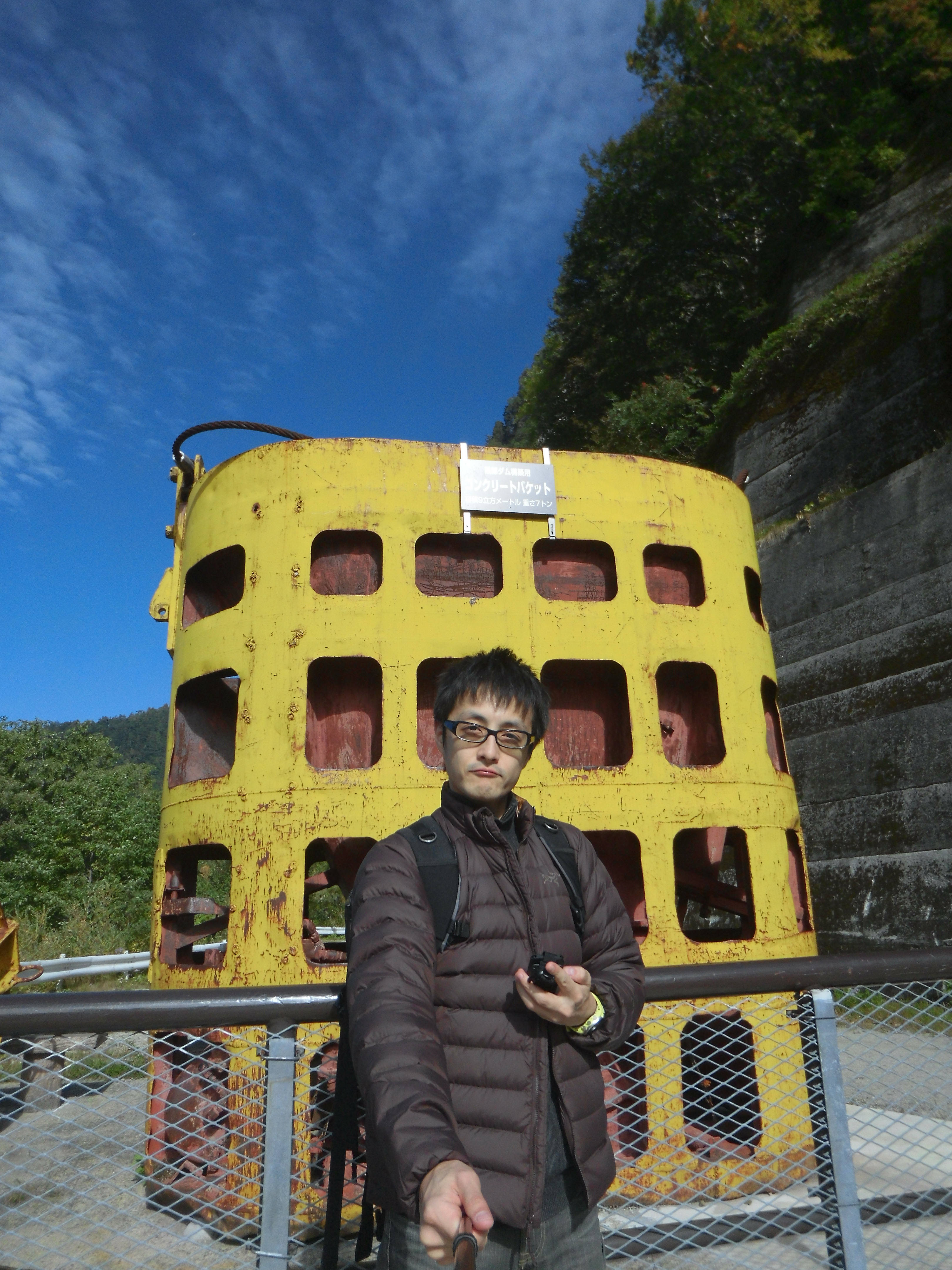 ポールの先にカメラを取り付けて自分撮りした場合。後ろにある黄色い物は黒部ダム建設時に使ったコンクリートバケットで、高さが3.63mもある。1/2,500秒 / F2.8 / ISO100 / オート / 3.8mm