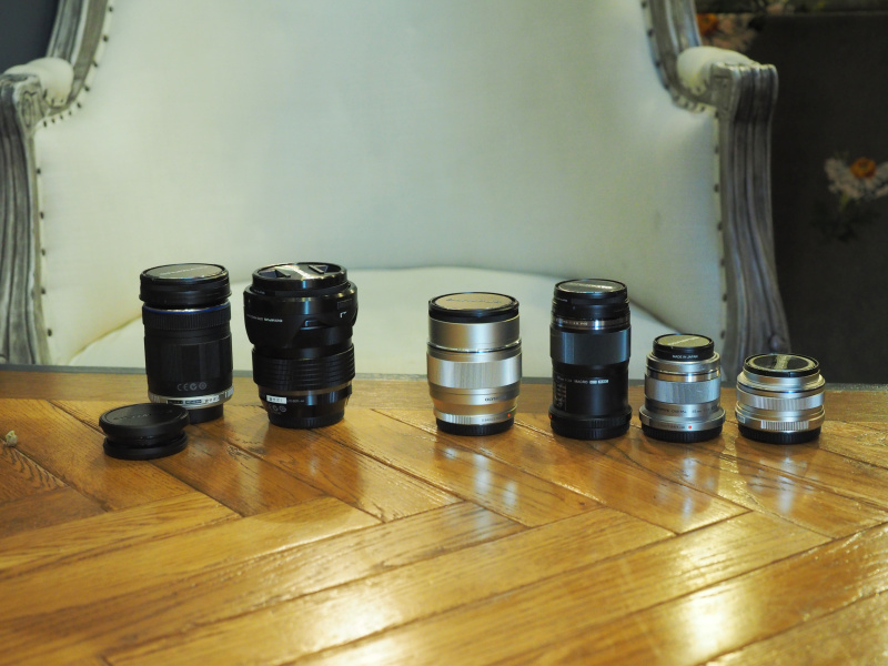 会場に並んだ交換レンズ。左から、ED 14-150mm F4.0-5.6、ED 12-40mm F2.8 PRO、ED 75mm F1.8、ED 60mm F2.8 Macro、45mm F1.8、17mm F1.8（名称の一部を省略）。