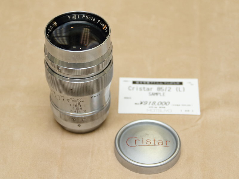 <strong class="">富士写真フイルムCristar 85mm F2 SAMPLE</strong><br class="">Cristar銘のレンズであるだけでも珍しいが、鏡筒にSAMPLEの文字が刻まれる。恐らくはマスコミなどの写真関係者、あるいはカメラ店などに一時的に貸し出されたものであろう。フロントキャップに描かれたCristarの書体もオシャレ。（フォトベルゼ）