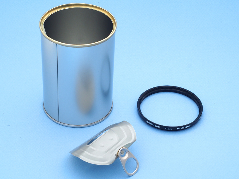 貯金缶は普通の缶詰と同じく、プルタブを引くとフタをパッカンと外すことができる。この開いた缶の口に、77mm径のフィルター枠（ジャンク品のガラスを外したもの）がすっぽりはまるのがミソである