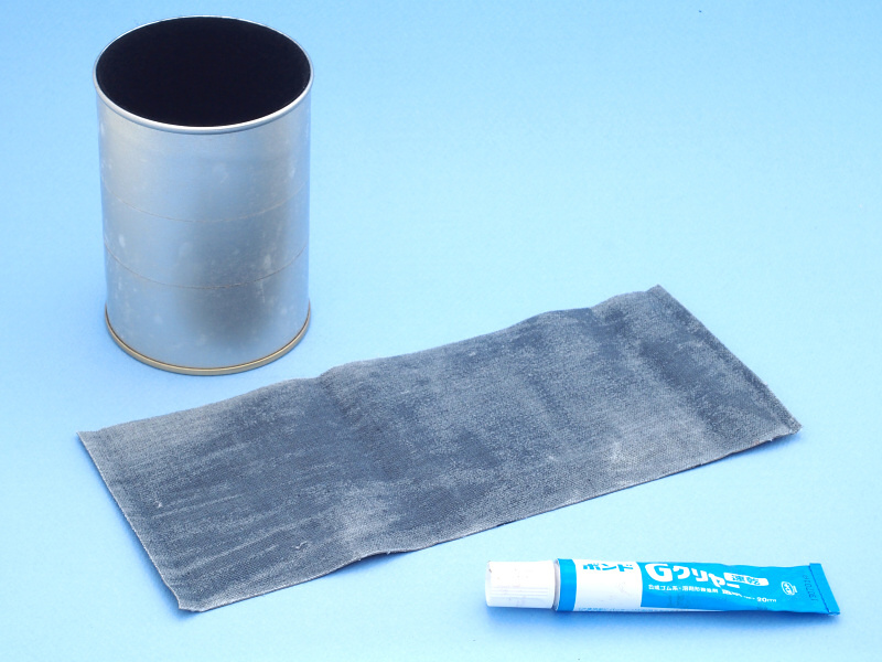 ポーチをばらして革だけにして、測ったサイズにカットする。しかし、この合成皮革は裏面が布地になっていて、両面テープで接着してもすぐ剥がれてしまう。そこでちょっと思案して、缶の表面に両面テープを貼り、布地にボンド「Gクリヤー」を塗布することにした。Gクリヤーを布地に薄く塗って乾かすと、両面テープへの食いつきが良くなると睨んだのである
