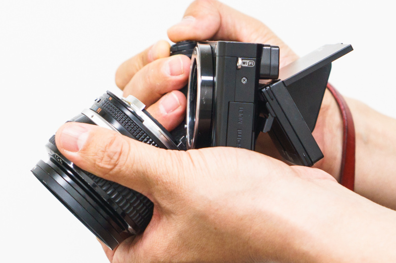 手のひらでレンズ下端を支えてレンズとカメラをへの字に曲げる。上の写真は左と同じ場所から撮影している