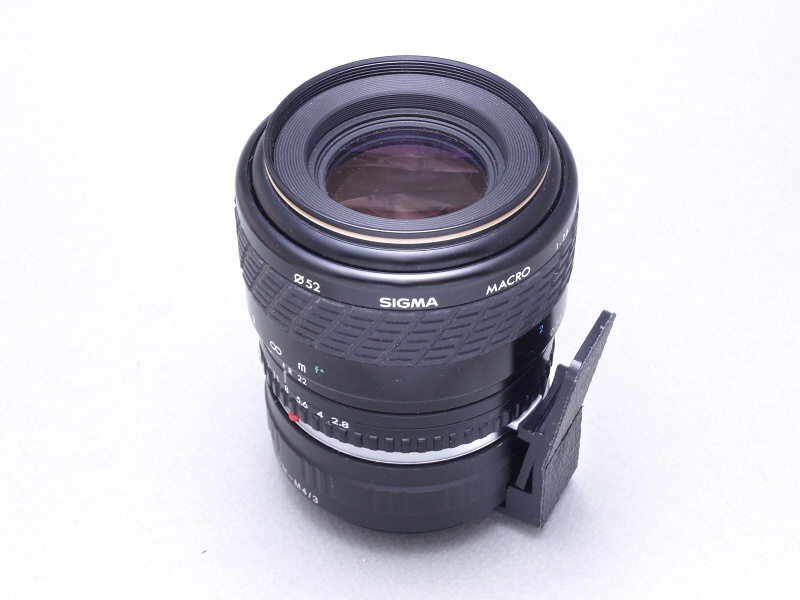 参考までに、同じOMマウントの「SIGMA MACRO 90mm F2.8」を装着したところ。実は同じOMマウントでも、メーカーによって絞り込みボタンの位置が若干のズレがある。この誤差を吸収するため、絞り込みレバーの幅に余裕を持たせている