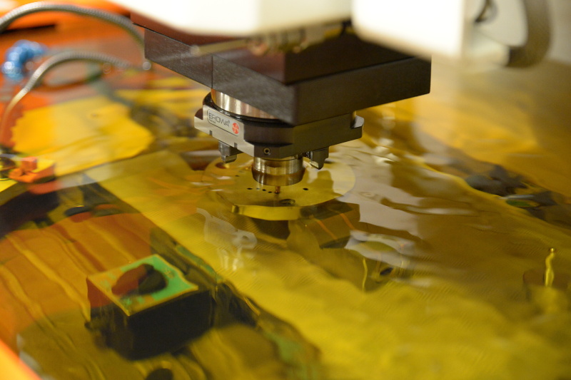 放電加工機は、加工する金型部品の周囲を油で満たし、その中で加工が行われる。時折ごく小さな火花が見えるが、研削加工のような音はしない