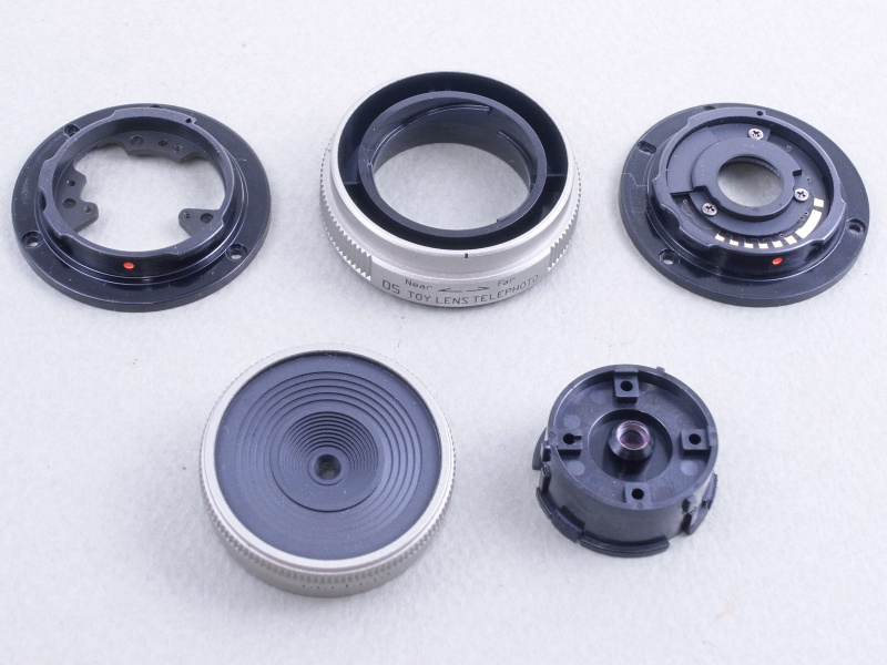 取りあえず05 TOY LENS TELEPHOTOのネジを外し、バラバラに分解してみる。レンズそのもの（右前）は非常に小さいが、大きめのレンズ枠パーツにはめ込まれ、これ以上は分解できない