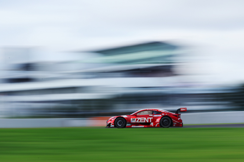 スローシャッターを使った流し撮り。背景にピットビルを入れてマシンのスピード感を表現してみた。<br>キヤノン EOS 7D Mark II / EF70-300mm F4-5.6L IS USM / 70mm（112mm相当） / マニュアル露出（F29、1/15秒）/ ISO 100