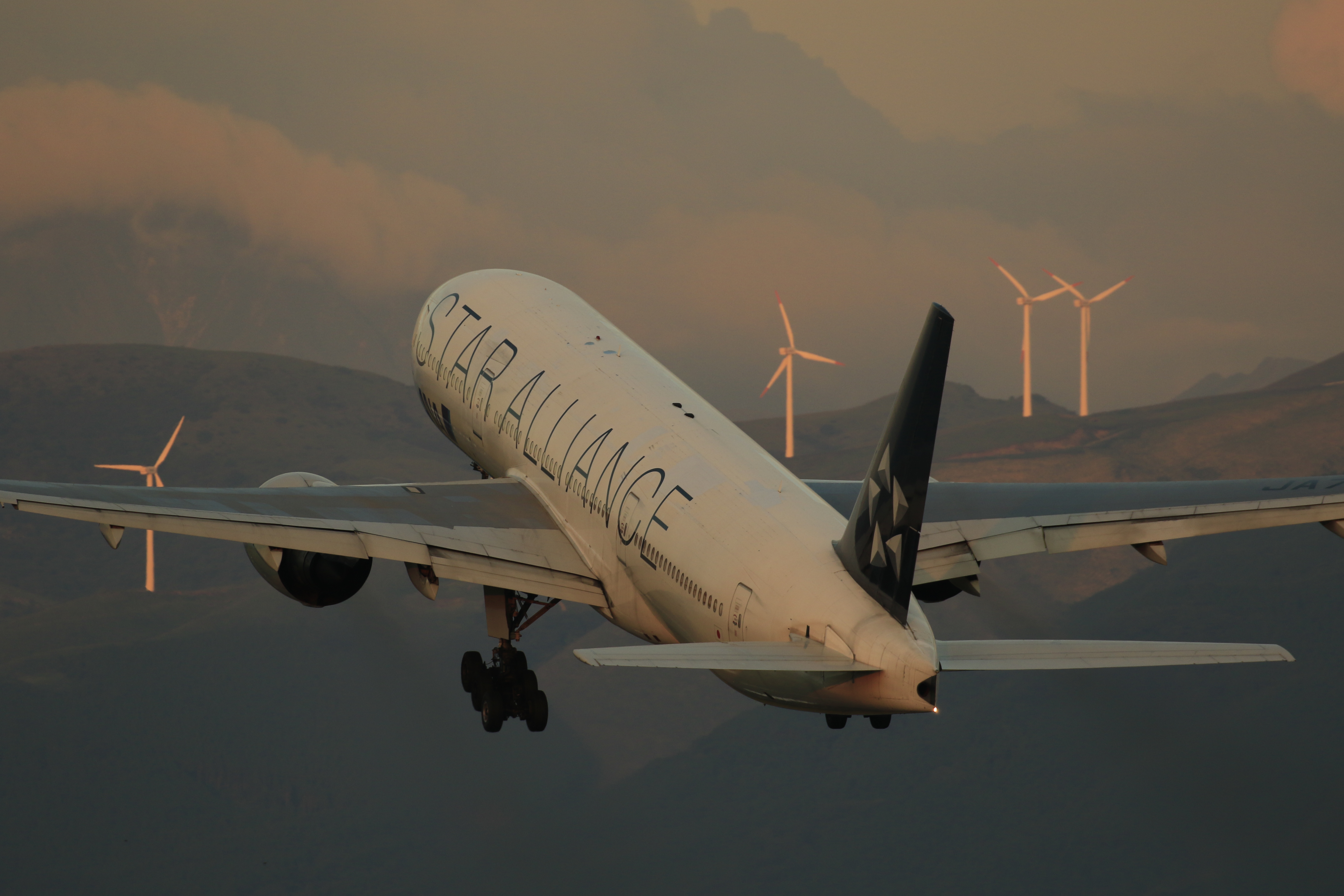 離陸する機体を背景にどう載せるか。この例ではちょうど風力発電の風車の間に機首が入ったタイミングを捉えることができた。必ずしも狙った通りに撮れるかわからないが、撮れるとそれだけ感動も深いのが航空機撮影の醍醐味だ。<br>キヤノン EOS 7D Mark II / EF100-400mm F4.5-5.6L IS II USM / 360mm（576mm相当） / 絞り優先AE（F6.3、1/500秒）/ ISO 200