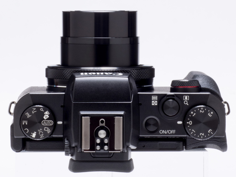 カメラ上面には大きなモードダイヤルと露出補正ダイヤルがそれぞれ独立して配置。他は電源ボタンとシャッターボタン、ズームレバーというシンプルな構成だ。いわゆる“ペンタ部”の左右側面に沿うようにマイクの小さな穴が見える
