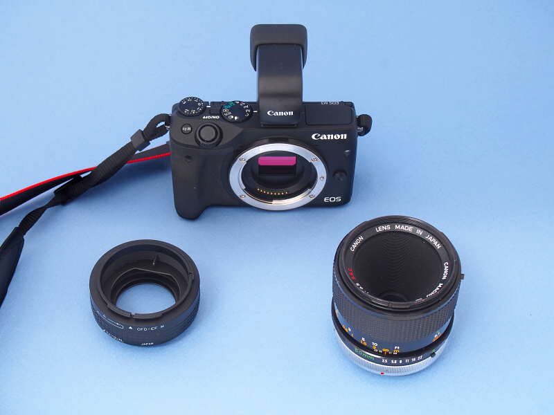 EOS M3に、<a href="http://homepage2.nifty.com/rayqual/EOS_M.html" class="n" target="_blank">RAYQUAL（宮本製作所）製のマウントアダプター</a>（左）を介して、MACRO FD 50mm F3.5（右）を装着する。MF時代のFDマウントレンズは、フランジバックの都合上、一眼レフカメラのEFマウントに装着すると無限遠が出なかった。しかしミラーレスカメラのEOS Mシリーズの登場によって、往年のFDレンズが最新のミラーレスカメラで楽しめるようになったのだ