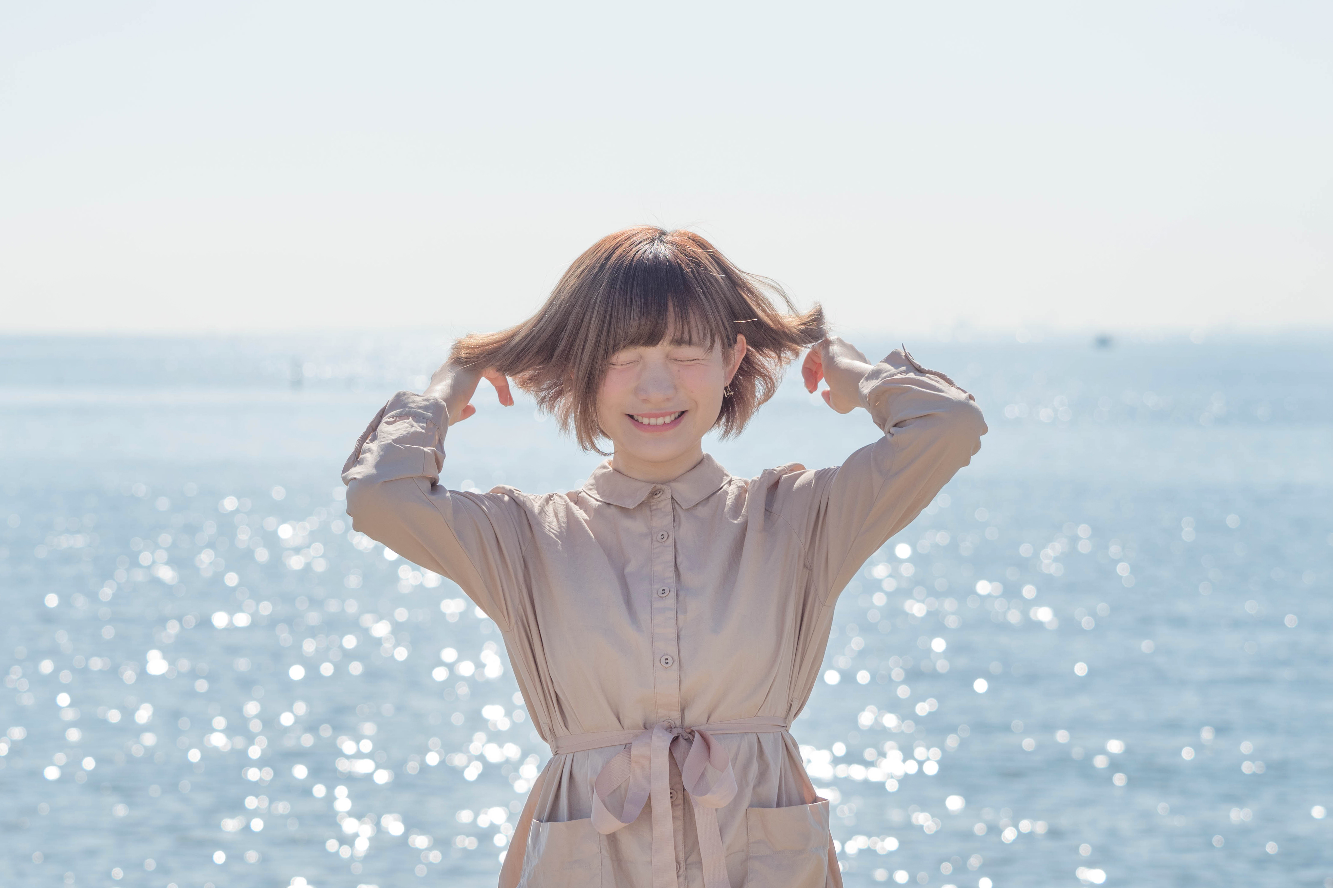 髪の毛を掻き上げる一瞬を、逆光で撮影。約10コマ/秒の連写のおかげで、会心の笑顔がとらえられた。9枚の絞り羽根（円形絞り）が作る煌めく海面の玉ボケが美しい。<br><span class="fnt-85">オリンパスOM-D E-M5 Mark II / M.ZUIKO DIGITAL ED 40-150mm F2.8 PRO / 60mm（120mm相当） / 絞り優先（F3.5、1/2,500秒、-0.3EV） / ISO200</span>