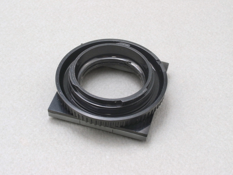 そこでアイデアを徹底するため、レンズもレゴで作ることにした。まず、マイクロフォーサーズカメラのボディキャップを丸くくり抜き、さらに正方形にカットしたABS板（2mm厚）に同じ大きさの穴を開け、両者を接着する。