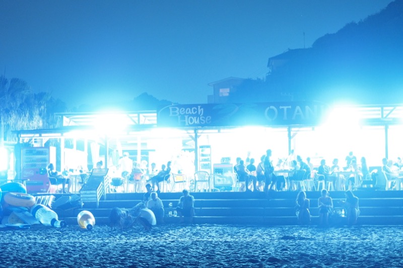 この日は花火大会で、海の家にはたくさんの人々が集った。シャッタースピード4段分の5軸手ブレ補正のおかげで、1.5秒のシャッター速度でも手ブレのない、シャープな描写が得られた。<br class=""><span class="fnt-85">オリンパス OM-D E-M1/ M.ZUIKO DIGITAL ED 12-40mm F2.8 PRO / 40mm（80mm相当） /マニュアル露出（F2.8、1.5秒） / ISO 1600</span>