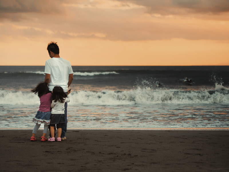 波が打ち寄せるたびに父親の後ろに隠れて楽しそうにはしゃいでいた子どもたち。夕暮れが3人を温かく照らしていたので開放絞りでやわらかさを強調。<span class="fnt-85">オリンパス OM-D E-M1 / M.ZUIKO DIGITAL 45mm F1.8 / 45mm（90mm相当） / 絞り優先AE（F1.8、1/640秒、-0.3EV） / ISO 200</span>