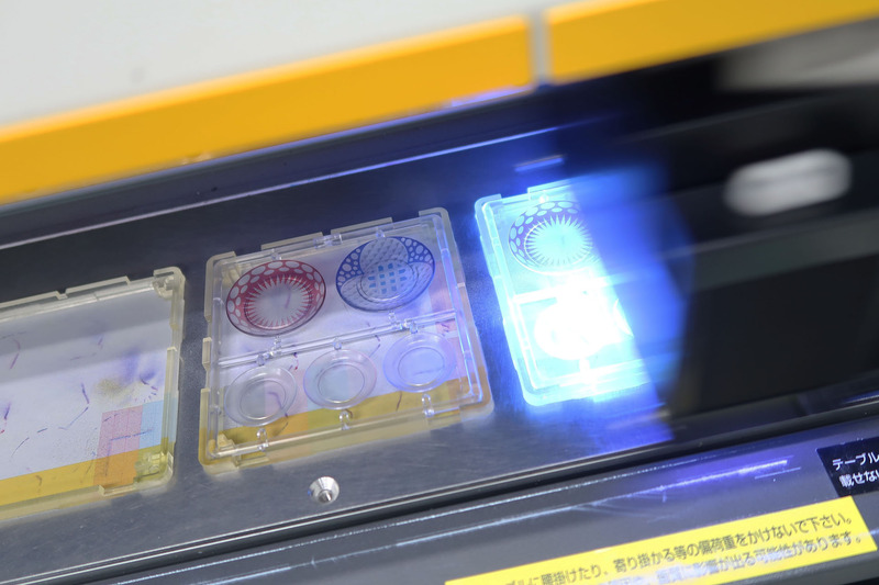 プラスチック樹脂にて射出成型されたランナーを、インクジェットプリンターにて彩色している風景（ちなみに1/12のお皿シリーズもイベントでテスト販売されているが、全国的な発売時期はまだ未定。ただし価格はやはり税別1,500円の予定だ）。エムアイシーが導入したインクジェットプリンターは相当に繊細な印刷が可能で、プロモデラーでも塗装再現が不可能なようなものが簡単に印刷できてしまう