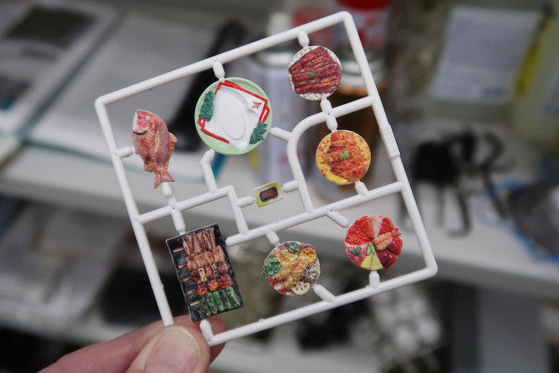 プラスチック樹脂にて射出成型されたランナーを、インクジェットプリンターにて彩色している風景（ちなみに1/12のお皿シリーズもイベントでテスト販売されているが、全国的な発売時期はまだ未定。ただし価格はやはり税別1,500円の予定だ）。エムアイシーが導入したインクジェットプリンターは相当に繊細な印刷が可能で、プロモデラーでも塗装再現が不可能なようなものが簡単に印刷できてしまう