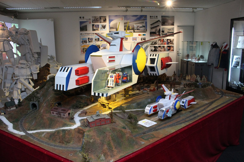 1/144スケールのホワイトベース。鉄道模型のスケールとも近く、下には線路が走る背景も。右手前に見えるホワイトベースは1/400スケール